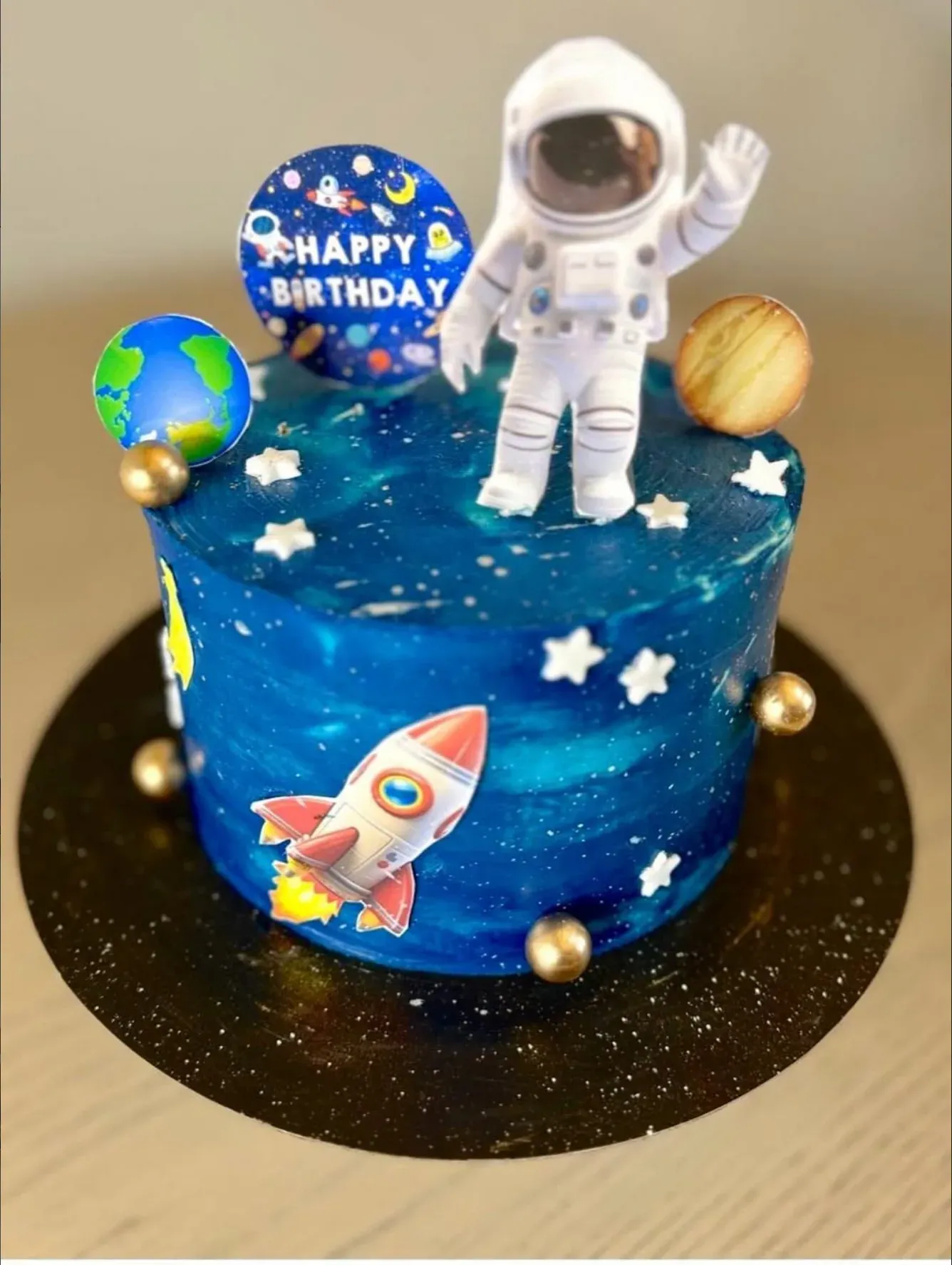 Deep blue galaxy-effect cake flecked with white stars, topped with a model astronaut and planets, with a rocket and Earth on the side.