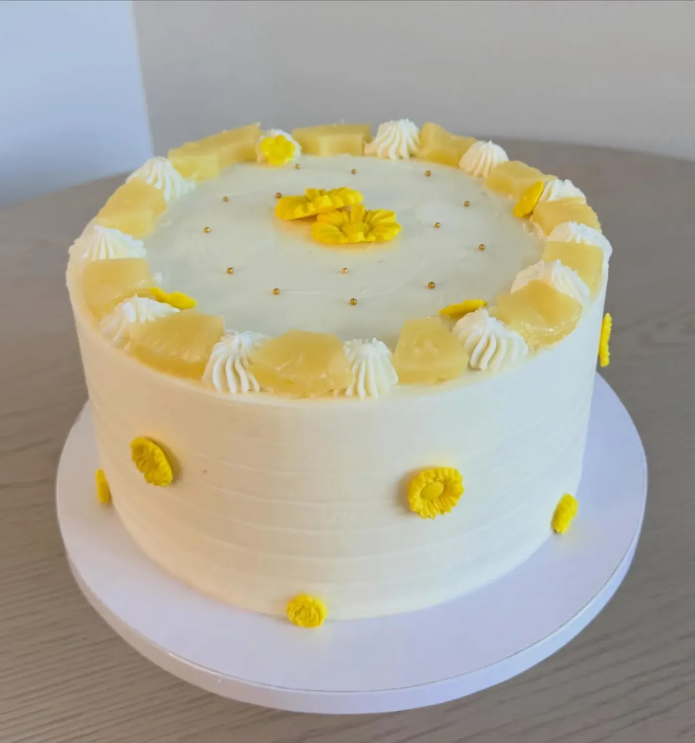 Pale lemon and cream cake with a ring of piped shells around the rim, finished with small yellow sugar flowers and gold dragees.