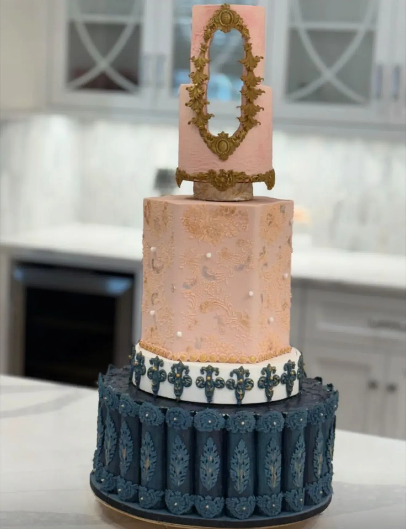 Three-tier Indian wedding cake: a deep teal base tier with scalloped gold mehndi-style panels, a blush tier piped with gold paisley and pearls, topped with a rose tier framed by an ornate gold baroque crest.