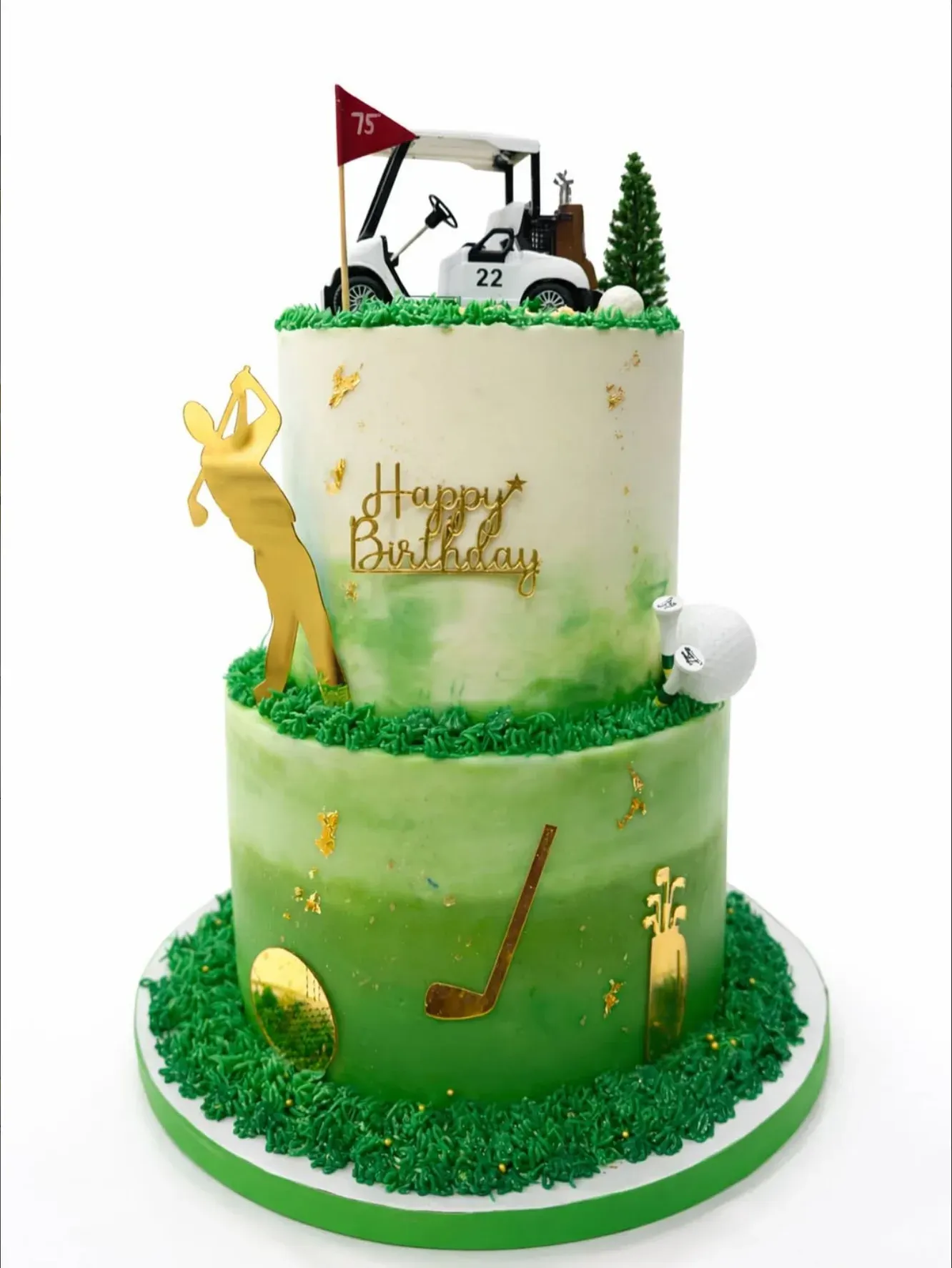 Two-tier cake with a green watercolor ombré lower tier, piped grass, gold golf-club and bag detailing, topped with a buggy, flag and sugar pine tree.
